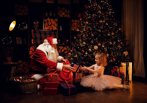 Little girl and Santa Claus unpack gifts while sitting by the Christmas tree Santa gives gifts to the child.